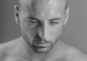 Male face with a short beard and strong jaw looking down