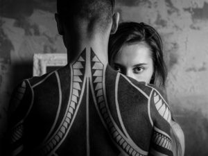 Woman peering over shoulder of tattooed man