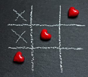 Three red hearts aligned in chalk board game of tic-tac-toe